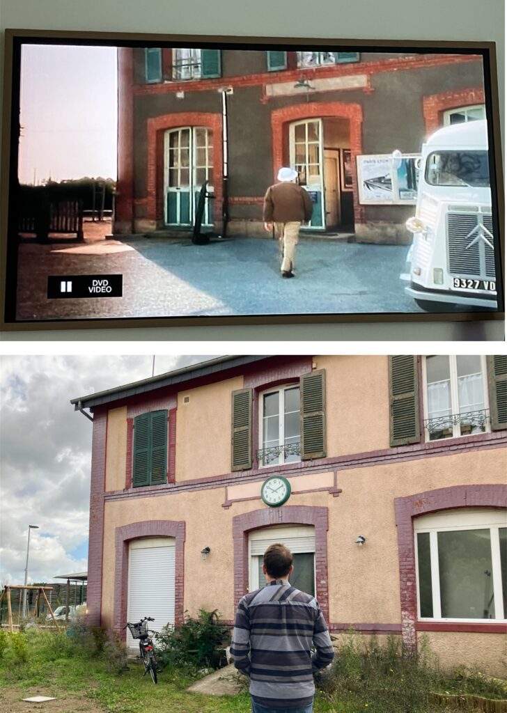 A split image showing a character walking towards a building from a scene in 'The Darling Buds of May' on a TV screen above and a person standing in front of the same building in real life below, featuring a clock on the wall.